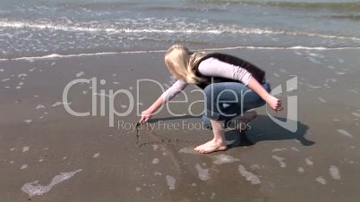 Blondine schreibt im Sand am Meer