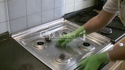 woman in gloves cleans a gas stove.
