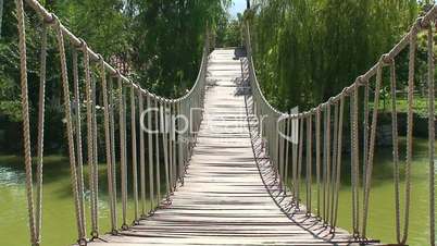 Old wooden rope bridge across a slimy pond