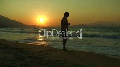 Man walks towards camera from waters edge at sunset