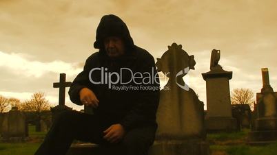 Hooded man sitting among gravestones