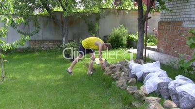 teenager carries stones for construction of flower bed.