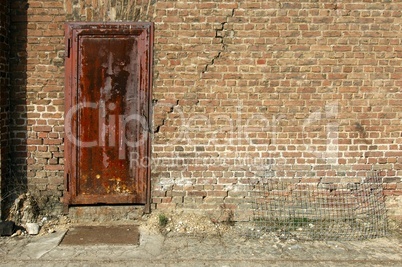 verrostete Tür an einer maroden Backsteinmauer