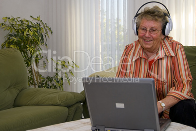 Oma mit Kopfhörer am Laptop