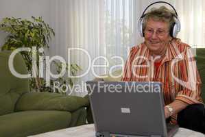 Oma mit Kopfhörer am Laptop