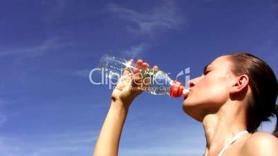 Young woman drinking water against the blue sky
