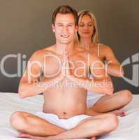 Young couple doing yoga on bed