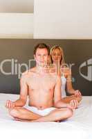 Young couple doing yoga on bed