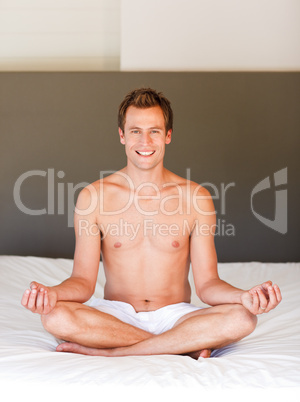 Smiling handsome man meditating on bed