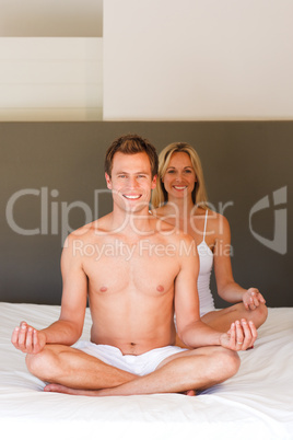 Smiling young couple doing yoga on bed