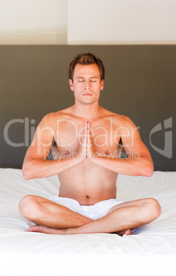 Handsome man meditating on bed with clossed eyes