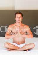 Handsome man meditating on bed with clossed eyes