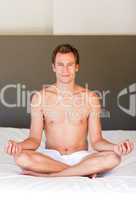 Handsome man meditating on bed
