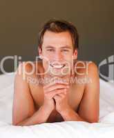 Young man relaxing in bed smiling at the camera