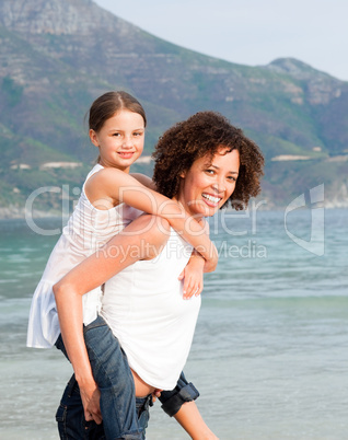 Mother giving daughter piggyback ride on the beach