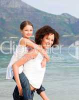 Mother giving daughter piggyback ride on the beach