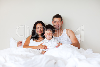 Couple and son together in bed smiling at the camera