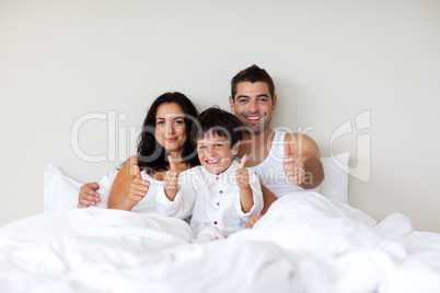 Little boy with thumbs up and his parents in bed