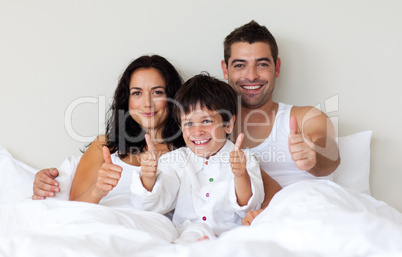 Happy son with thumbs up and his parents in bed