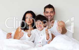 Happy son with thumbs up and his parents in bed