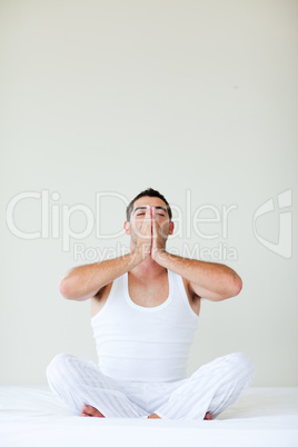 Young man doing yoga sitting in bed