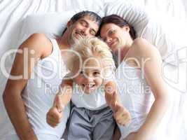 Happy little girl on bed with thumbs up and her parents
