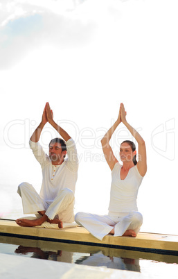 Man and woman doing yoga near the sea