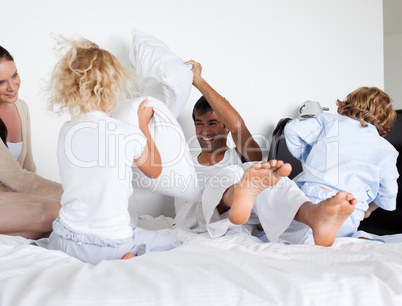 Parents and children playing with pillows on bed