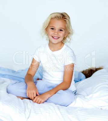 Little girl in bed smiling at the camera while her brother is sl