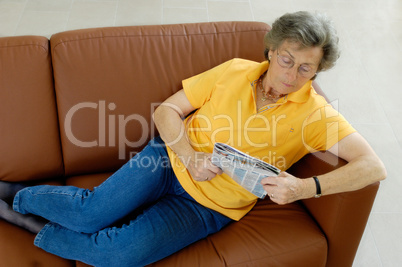 Seniorin liegt lesend auf einer Couch