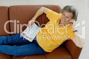 Seniorin mit Telefon und Zeitschrift auf einer Ledercouch