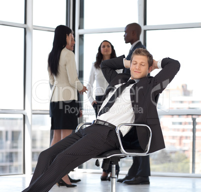 manager relaxing in office with team in background