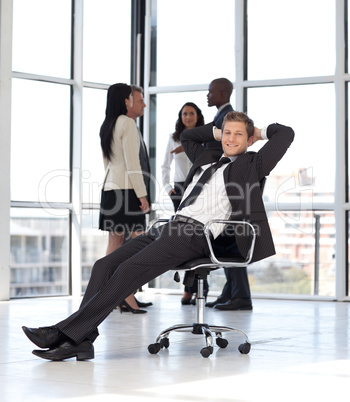 manager relaxing in office with team in background