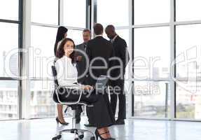 woman sitting in office working with team in background