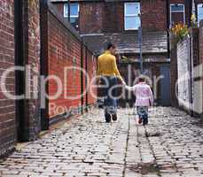 Young mother and daughter walking down cobblestone alley