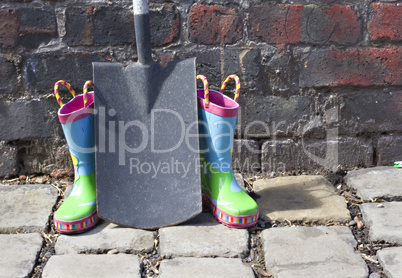 Childs wellington boots and shovel against an old brick wall