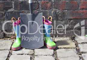 Childs wellington boots and shovel against an old brick wall