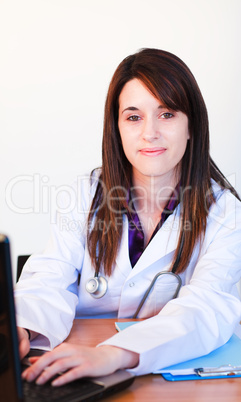 Brunette doctor using a laptop and smiling at the camera