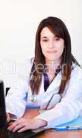Brunette doctor using a laptop and smiling at the camera