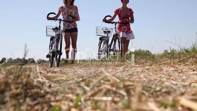 zwei Mädchen schieben ihre Fahrräder über einen Feldweg