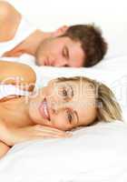 Couple lying in bed and woman smiling at the camera