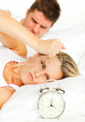Man and angry woman in bed looking at the alarm clock going off