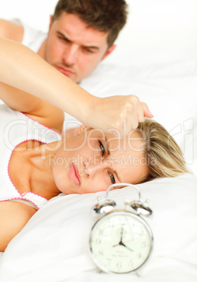 Man and angry woman in bed looking at the alarm clock going off