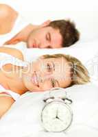 Couple in bed with alarm clock and woman smiling at the camera