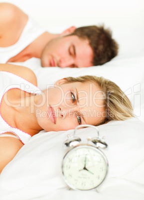 Couple in bed and angry woman looking at the alarm clock