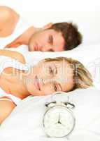 Couple in bed with alarm clock and woman smiling at the camera