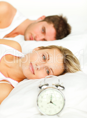 Woman lying with her boyfriend looking at the alarm clock