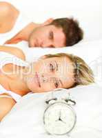 Woman lying with her boyfriend looking at the alarm clock