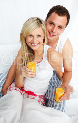 Couple holding orange juice glasses in bed