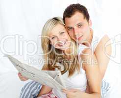 Couple reading a newspaper in bed and smiling at the camera